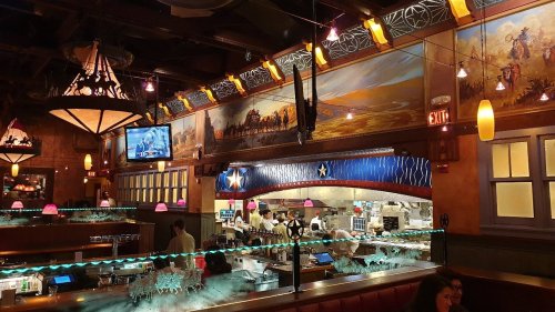 Interior of a restaurant featuring a bar, colorful lighting, and a mural depicting a western scene.