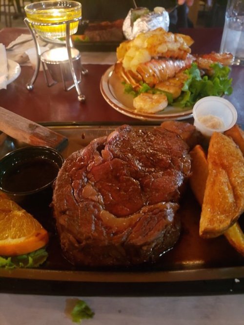 A juicy steak with a side of golden fries and an orange slice, served on a sizzling platter.
