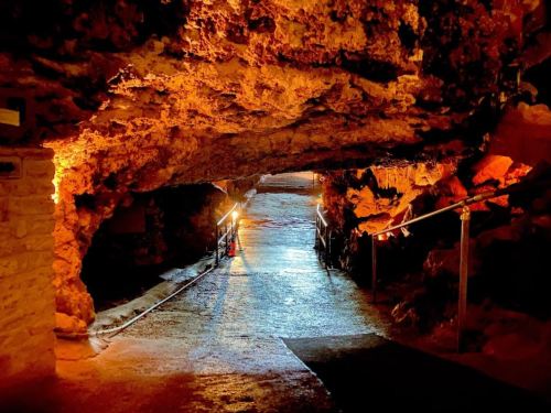 A dimly lit cave pathway with rocky walls and a smooth floor, illuminated by soft lights along the sides.