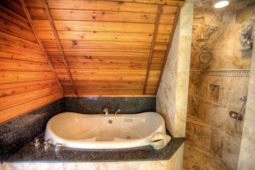 A luxurious bathroom featuring a jetted tub and a separate shower with stone walls and a wooden ceiling.