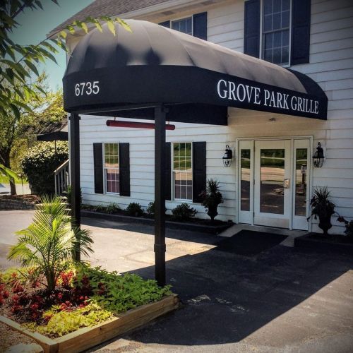 Entrance of Grove Park Grille featuring a black awning, white building, and landscaped flower beds.
