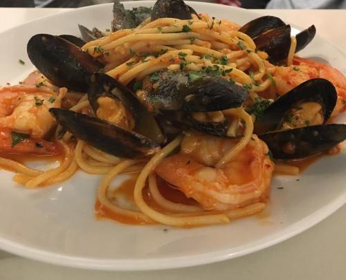 A plate of spaghetti topped with shrimp, mussels, and herbs in a rich tomato sauce.