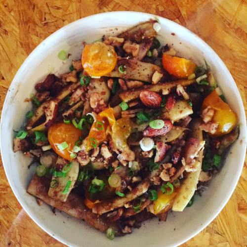 A bowl of mixed vegetables, nuts, and green onions, featuring orange and yellow tomatoes on a wooden surface.