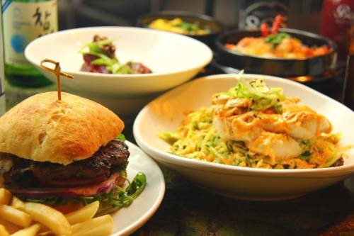 A delicious spread featuring a burger with fries, a bowl of noodles, and two other dishes garnished with herbs.