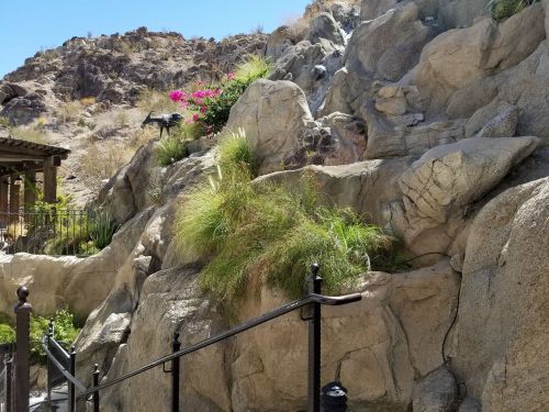 A rocky landscape with vibrant flowers and greenery, featuring a railing leading up a path.