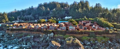 A row of coastal houses perched on a cliff, surrounded by trees and overlooking the ocean.