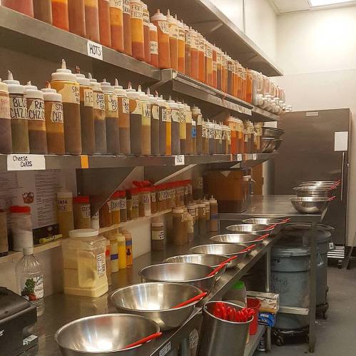 A kitchen shelf filled with labeled condiment bottles and metal bowls arranged on a counter.