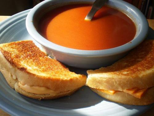 A bowl of tomato soup with two grilled cheese sandwiches on a blue plate.