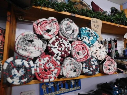 A stack of rolled blankets in various colors displayed on a wooden shelf, with greenery above and a sign nearby.