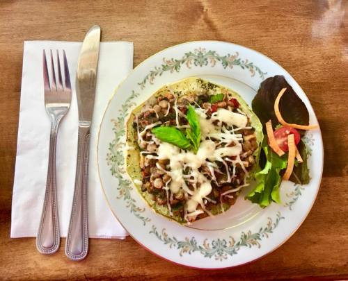A plate with a taco topped with meat, cheese, and herbs, accompanied by salad and utensils on a wooden table.