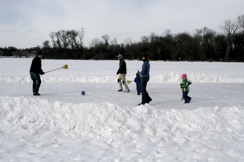 A family enjoys a winter day on a frozen lake, playing and walking on the ice surrounded by snow.