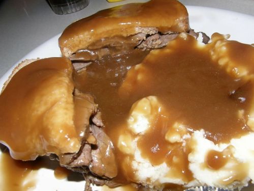 A plate of mashed potatoes topped with gravy and a sandwich filled with beef and gravy.