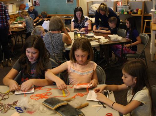 Children and adults engaged in a crafting activity, working on projects at tables in a creative space.