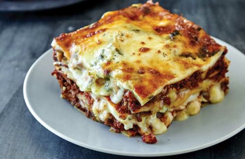 A slice of lasagna on a gray plate, featuring layers of pasta, meat sauce, and melted cheese.