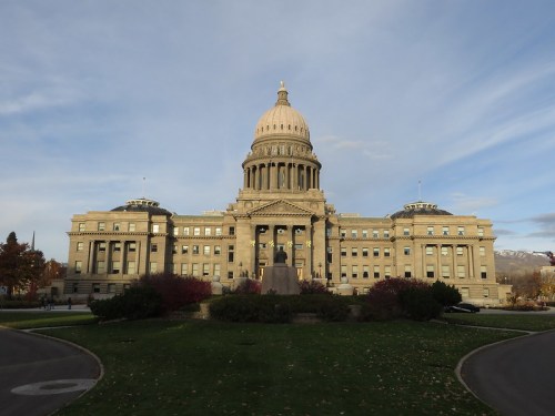 Idaho State Capitol building with a large dome, surrounded by greenery and a clear blue sky.