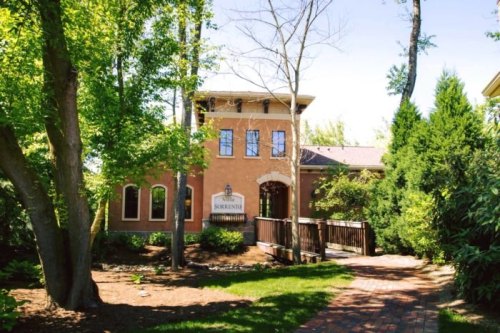 A charming building surrounded by trees and greenery, featuring a welcoming entrance and a pathway leading up to it.