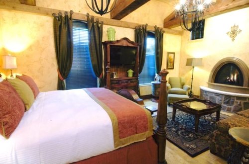 Cozy bedroom with a king-sized bed, fireplace, armchair, and wooden accents, featuring warm lighting and elegant decor.
