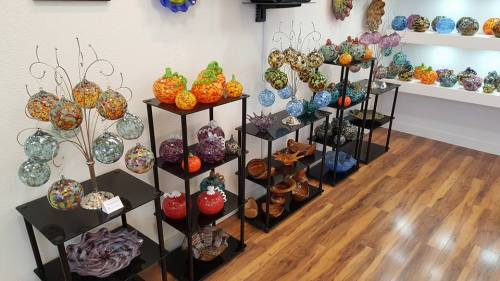 Colorful glass art displayed on black shelves, featuring decorative orbs, pumpkins, and various glass bowls.