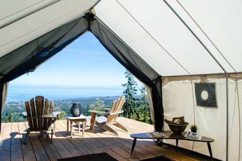 A cozy tent interior with two chairs and a table, overlooking a scenic view of trees and water.