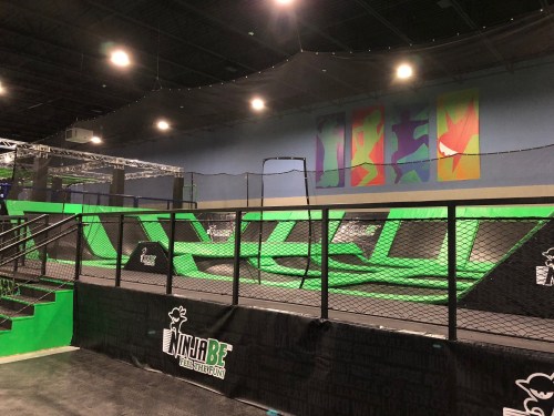 Indoor trampoline park featuring green trampolines, safety nets, and colorful wall art.