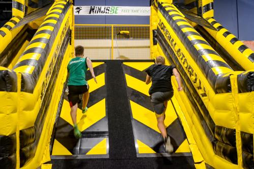 Two people running up inflatable slides with yellow and black stripes in a fun indoor activity center.