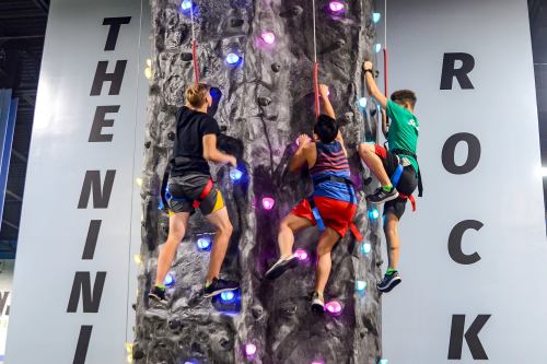 Three climbers ascend a colorful indoor rock wall, showcasing their skills and teamwork.