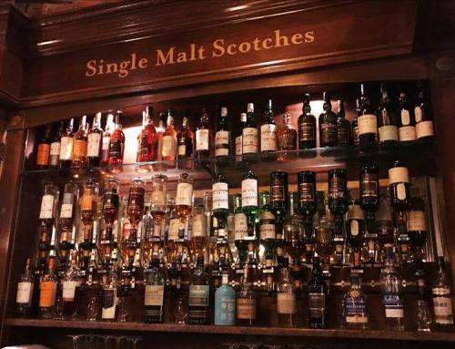 A wooden shelf displaying a variety of single malt Scotch whisky bottles.