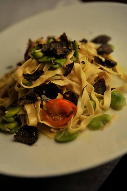 A plate of fettuccine pasta topped with black truffles, green beans, and cherry tomatoes.