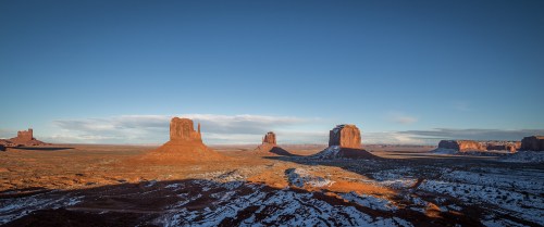 A scenic view of Monument Valley, featuring iconic sandstone buttes under a clear blue sky.