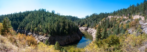 A panoramic view of a river winding through a forested landscape with rocky cliffs and vibrant autumn foliage.