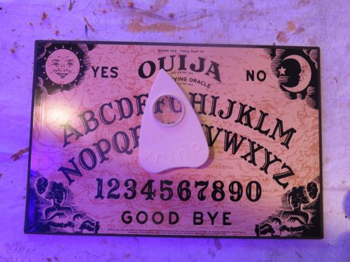 A Ouija board with a planchette on top, featuring letters, numbers, and the words "Yes," "No," and "Good Bye."