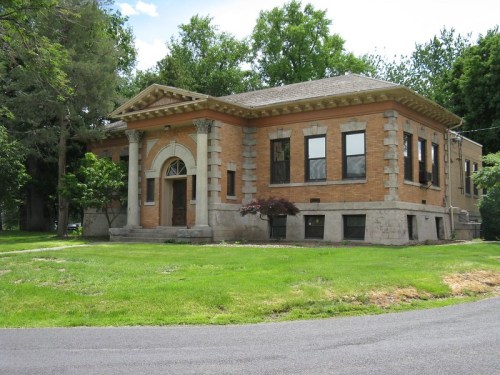 Historic brick building with a decorative entrance, surrounded by green grass and trees under a blue sky.