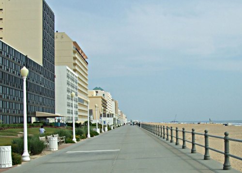 A wide boardwalk lined with hotels, leading to a sandy beach under a clear sky.