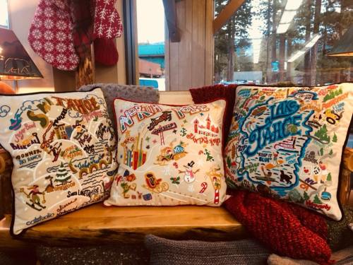 Three decorative pillows with colorful, embroidered designs featuring winter sports and mountain themes, arranged on a bench.