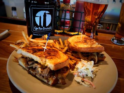 A plate with a grilled sandwich, fries, and coleslaw, alongside a beer and a bottle from Cape Pro Brewing Co.