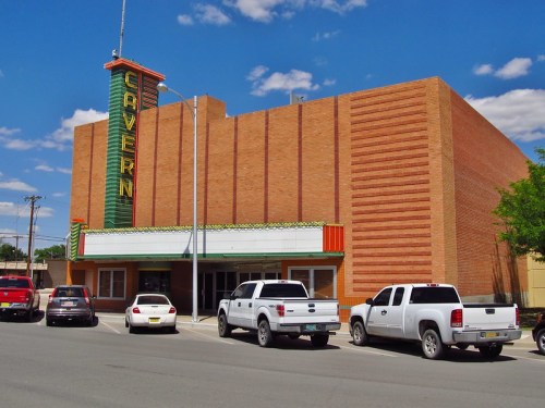 Exterior of the Cavern Theater, featuring a brick facade and colorful marquee, with parked cars in front.