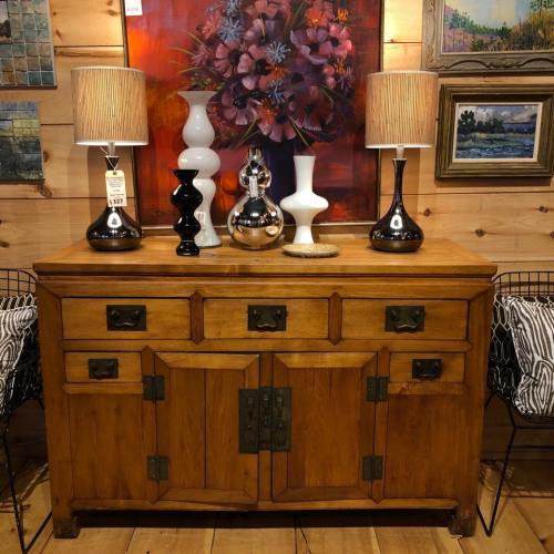 A wooden sideboard with decorative lamps and vases, set against a colorful wall of artwork.