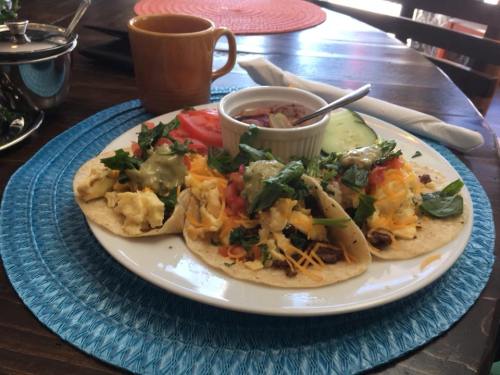 A plate of tacos filled with eggs, cheese, and vegetables, served with a side of salsa and garnished with fresh herbs.