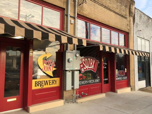 Exterior of a brewery and pizza joint with red doors and striped awnings, featuring colorful signage.