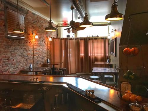 Cozy restaurant interior with exposed brick walls, warm lighting, and wooden tables, featuring a bar area in the foreground.