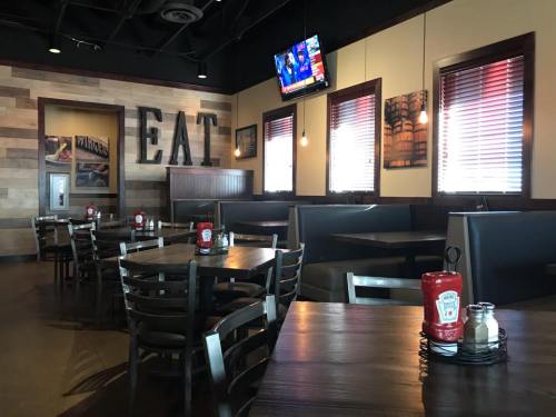 Interior of a restaurant featuring wooden decor, tables with ketchup bottles, and a TV displaying news.
