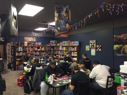 A cozy game store with people playing tabletop games, surrounded by shelves of board games and festive lights.