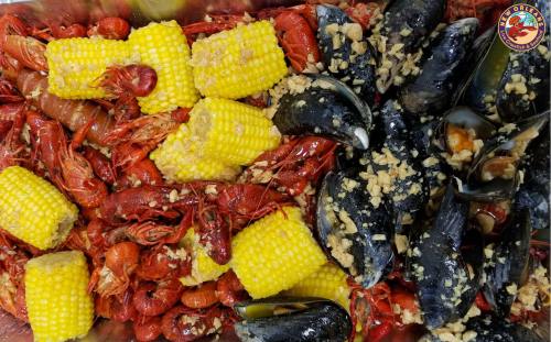 A tray filled with red crawfish, yellow corn, and black mussels topped with garlic.