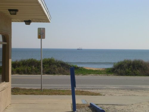 A view of the ocean from a building, with a distant ship on the water and a clear blue sky above.