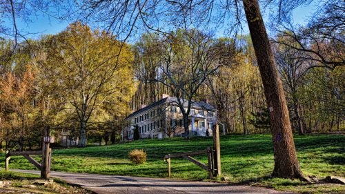 A historic stone house surrounded by trees and greenery, with a clear blue sky in the background.