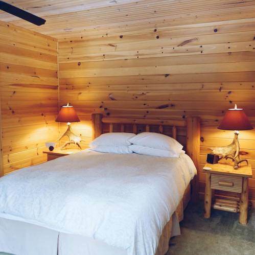 Cozy bedroom with a wooden bed, two lamps, and warm wooden walls, creating a rustic and inviting atmosphere.