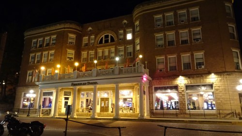 Historic hotel facade at night, featuring bright lights and a welcoming entrance with outdoor seating.