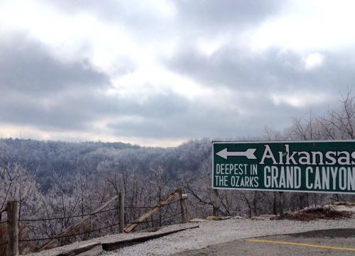 Signpost indicating "Arkansas Grand Canyon" with a scenic, frosty landscape in the background under a cloudy sky.