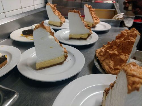 Slices of meringue pie on white plates, arranged on a kitchen counter.