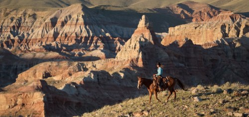 A rider on horseback traverses a rugged landscape of colorful rock formations under a clear sky.